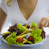 Une jeune femme devant une assiette de légumes et fruits.