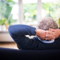 Un homme assis dans son canapé, regardant dans son jardin à travers la fenêtre vitrée (Photo : Unsplash).